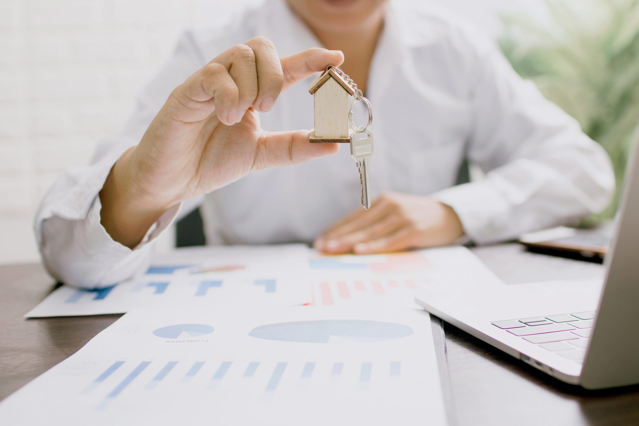person holding a small house model over a desk with document